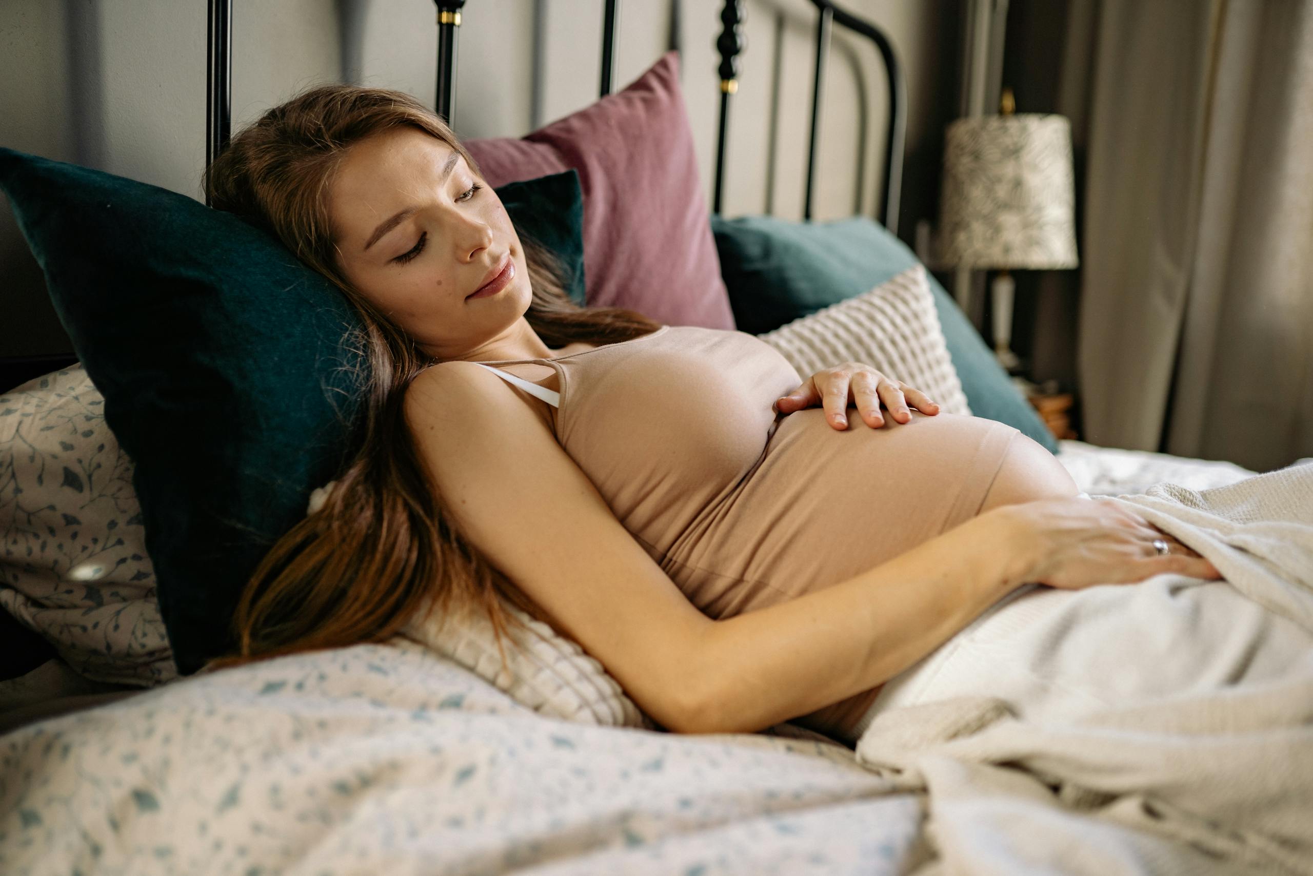 Pregnant Woman Lying on the Bed while Looking at Her Baby Bump